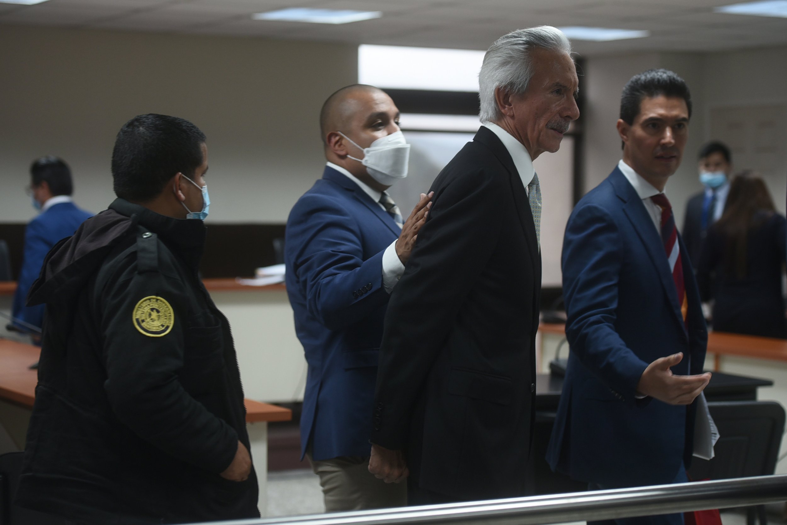 José Rubén Zamora es conducido por un custodio dentro de una sala de tribunales.