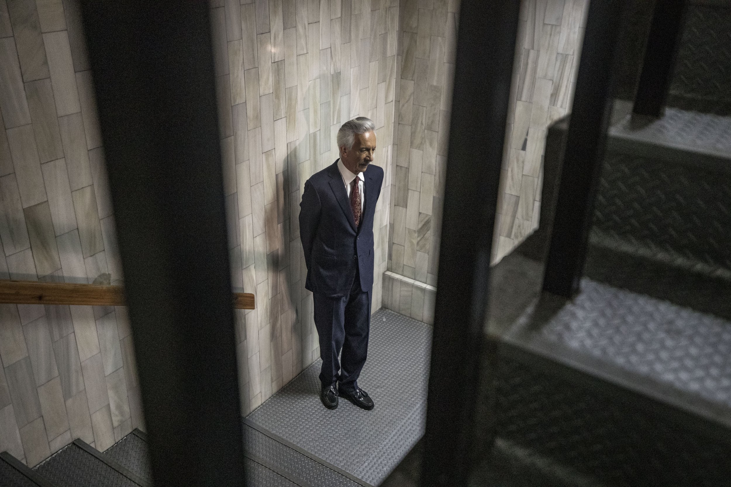 José Rubén Zamora, de traje, espera solo en un rellano de escaleras del edificio judicial.