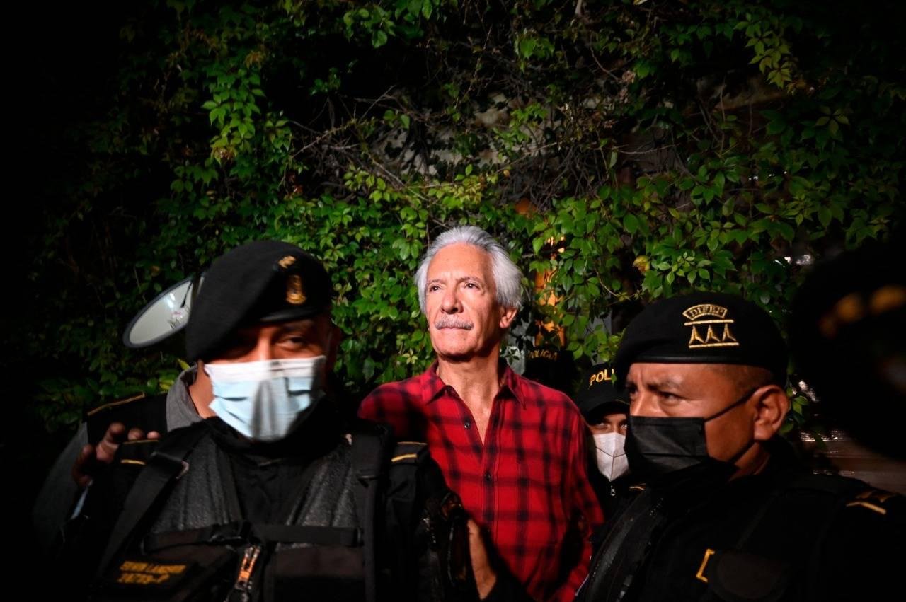 José Rubén Zamora, con camisa de cuadros roja, es escoltado de noche por agentes de la policía guatemalteca.